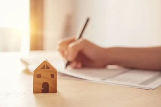 baurecht-recht-bau-gesetz-versicherung-haus-11 Holzspielzeug Haus mit Frau unterzeichnet einen Kaufvertrag oder Hypothek für ein Haus, Immobilien-Konzept.