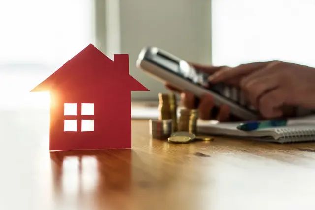 Hauskauf planen mit sicherem Eigenkapital Modellhaus neben Taschenrechner und Münzen auf Schreibtisch als Symbol für sichere Eigenkapitalplanung beim Hausbau